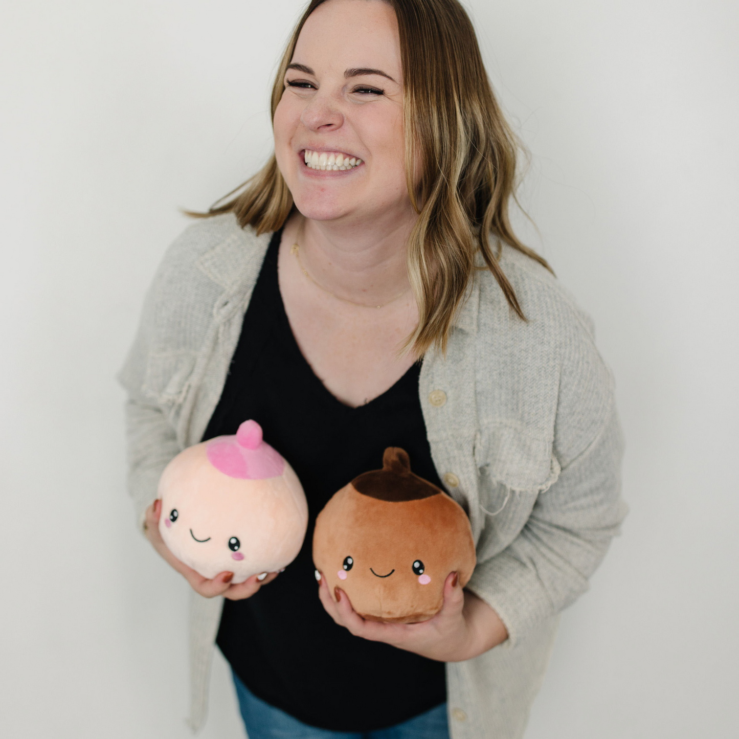 Smiling woman holding an ivory and tan breast plushies