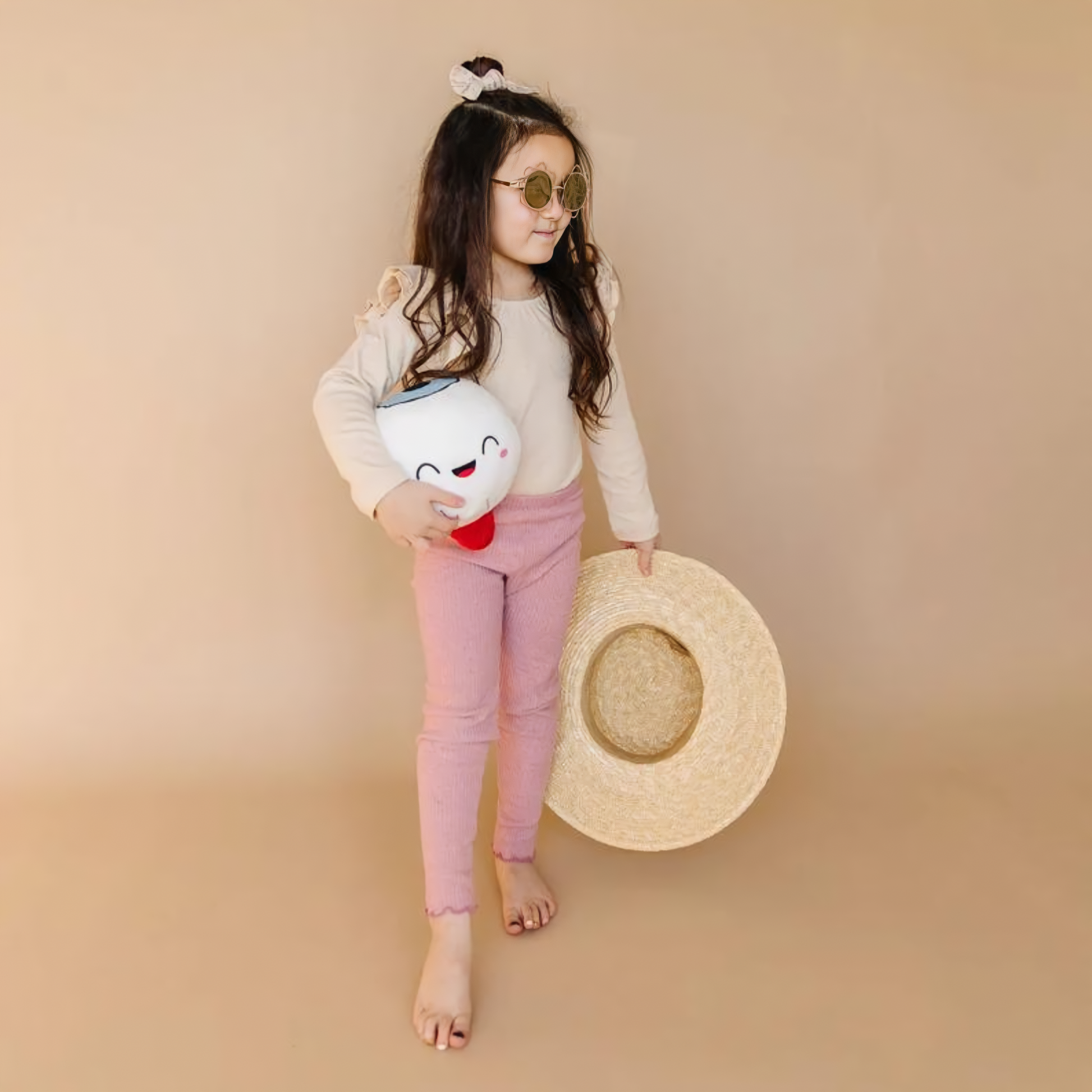 girl wearing a sunglass holding a hat and eye toy plushie