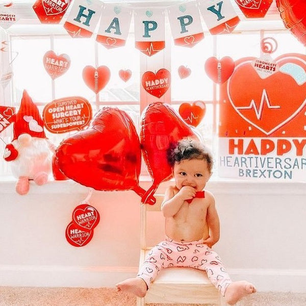 Toddler sitting on a chair with red heart balloons on background