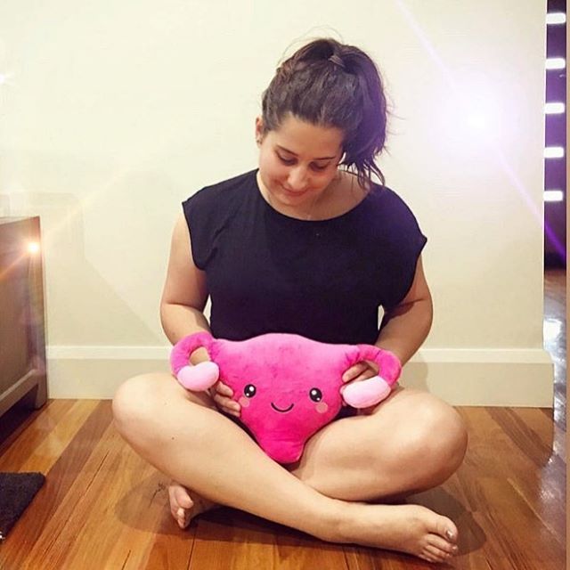 Lady sitting on the floor holding the Uterus Plushie