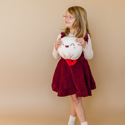 standing little girl in a red dress holding a nerdbugs eye organ plushie