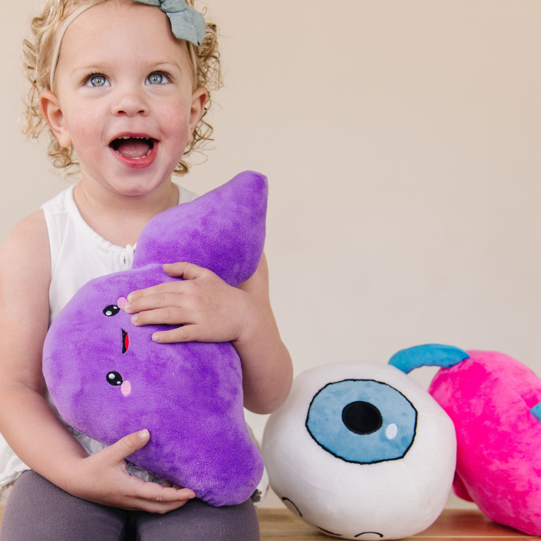Child hugging a Nerdbugs liver plushie while sitting beside Nerdbugs eye and heart plushies
