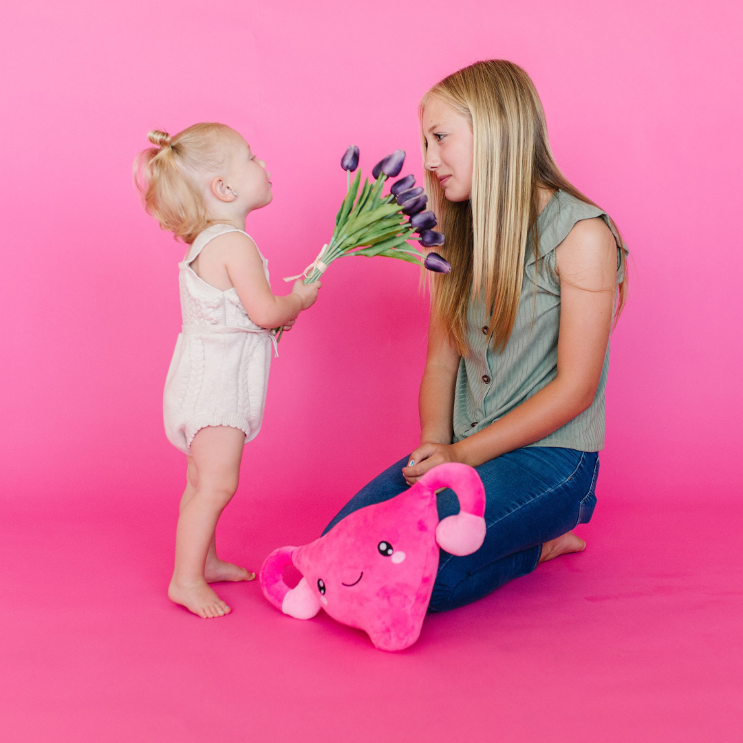 Young child offering purple tulips to an older girl who is kneeling on the floor with a Nerdbugs heart plushie in front of her