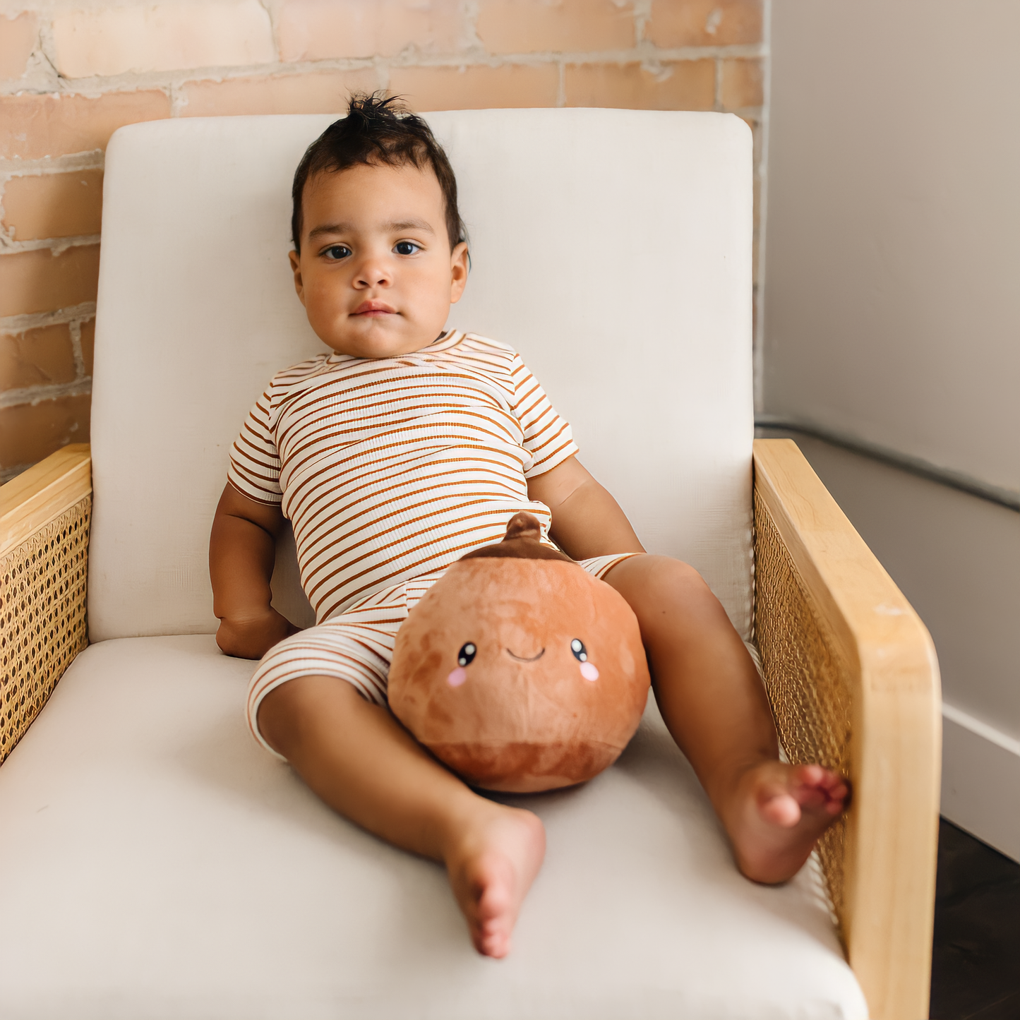 baby boy sitting on a white wooden chair with a tan breast plushie